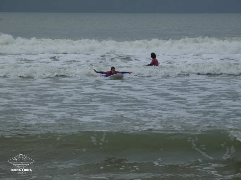 une dame qui glisse allongé avec une planche de surf dans la mousse en lachant les bras.